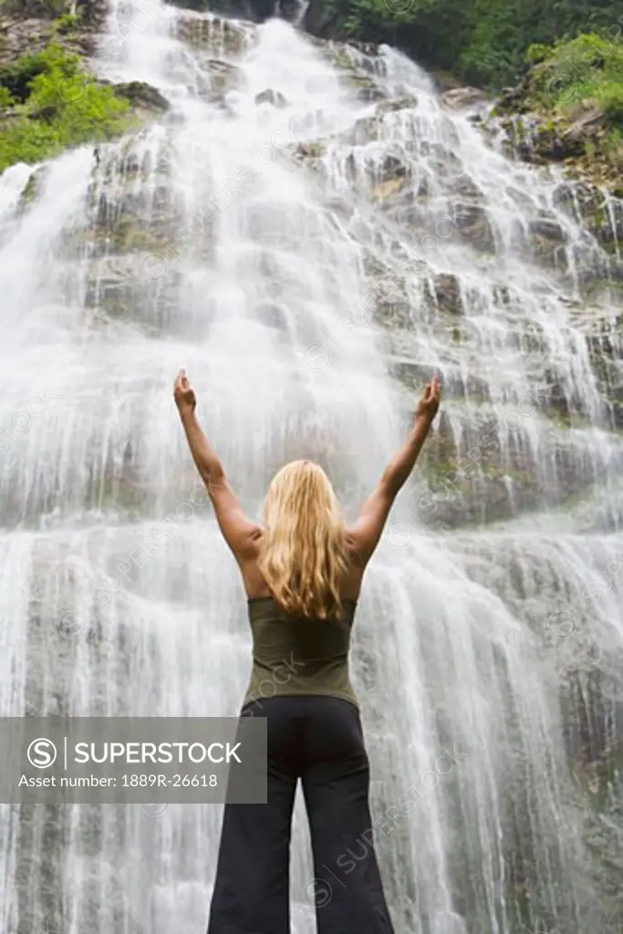 Woman with arms raised at the foot of a waterfall