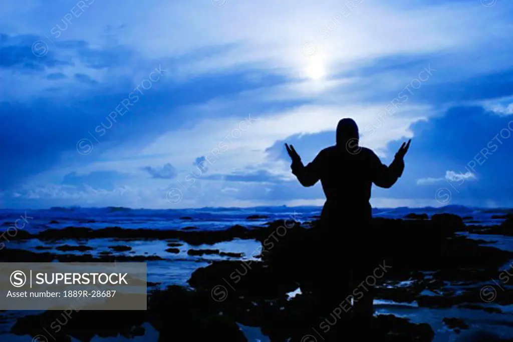 Silhouetted figure of someone worshipping by the ocean