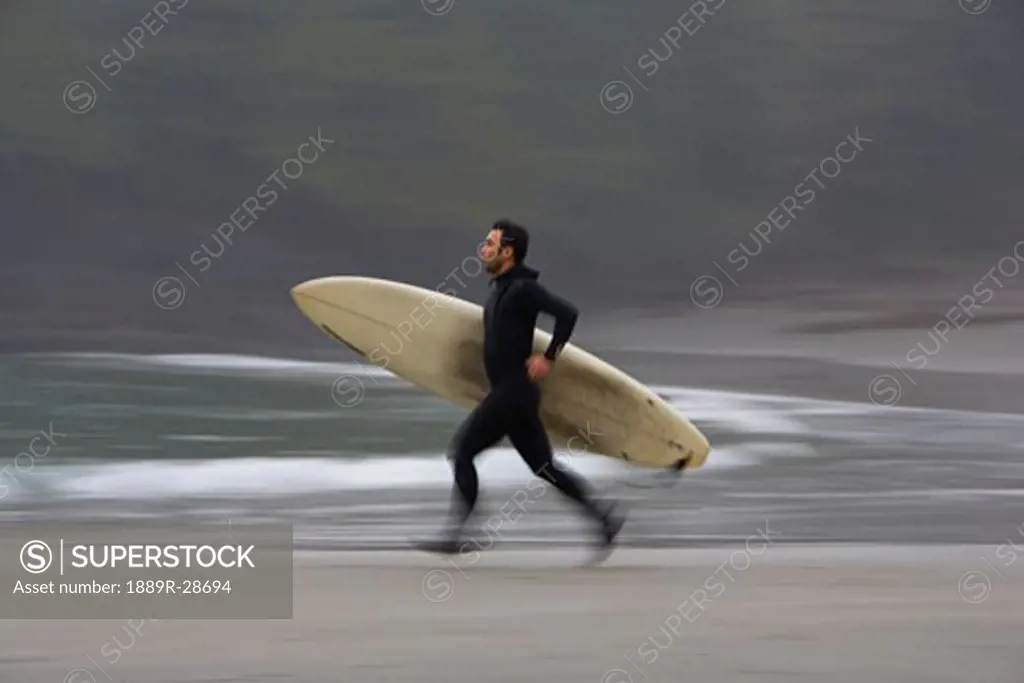 A surfer running to the water with his board