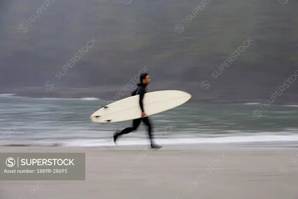 A surfer, running with board along the shoreline