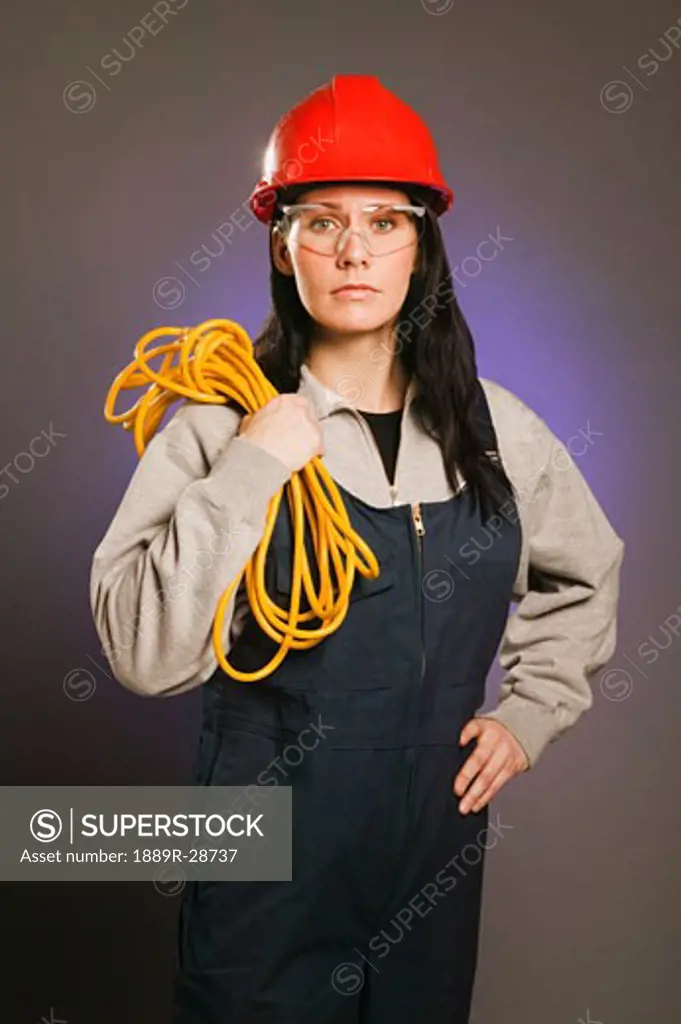 Tradeswoman in coveralls, carrying an extension cord