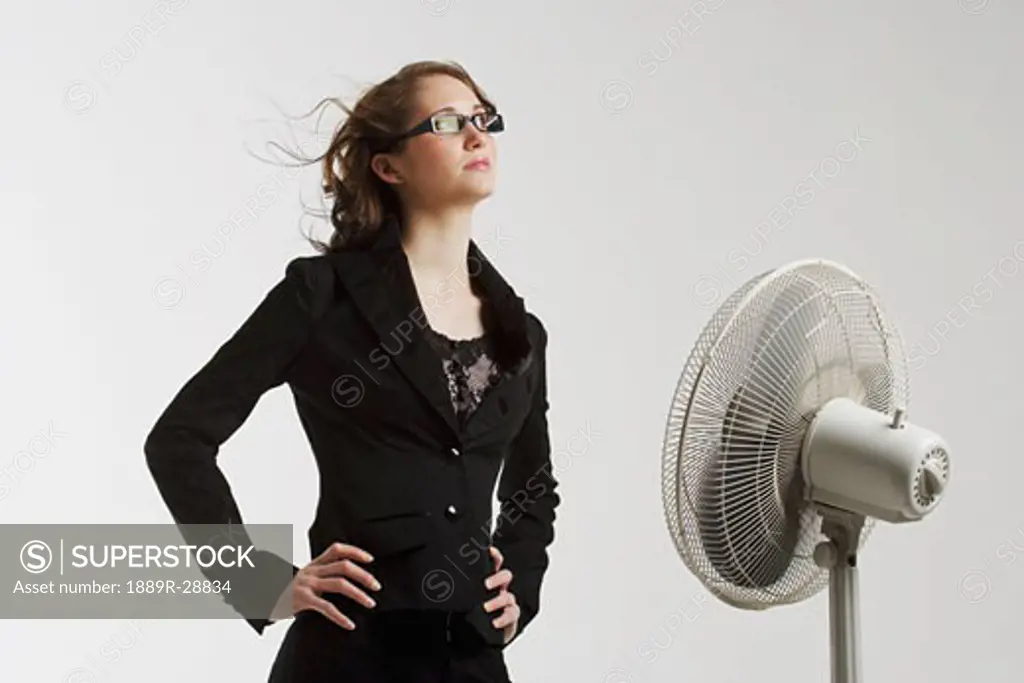 Young woman standing in front of an electric fan