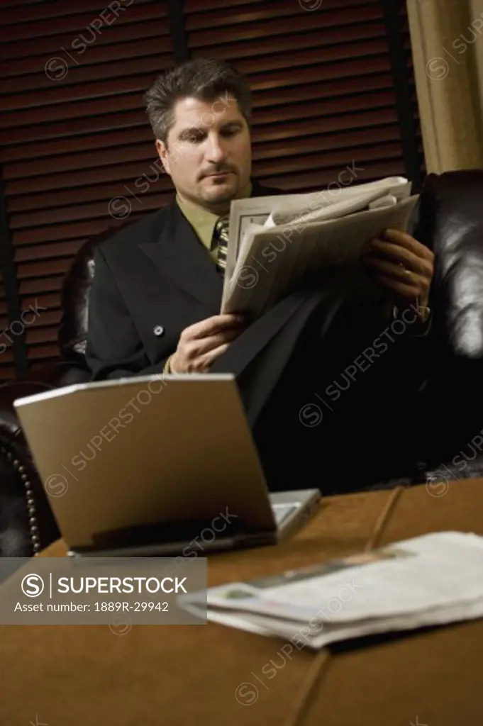 Businessman reading the newspaper with his laptop
