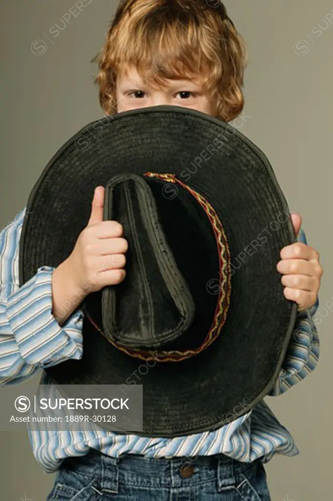 Young boy hiding part of face with large cowboy hat