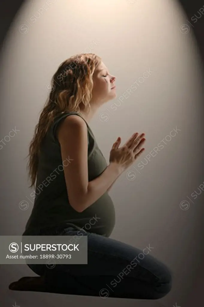 Side view of a pensive pregnant woman sitting in the prayer position