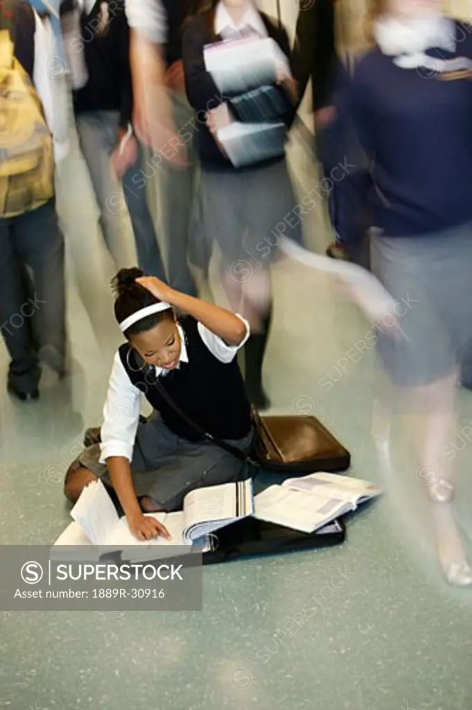 Teenage girl doing homework in middle of school hall