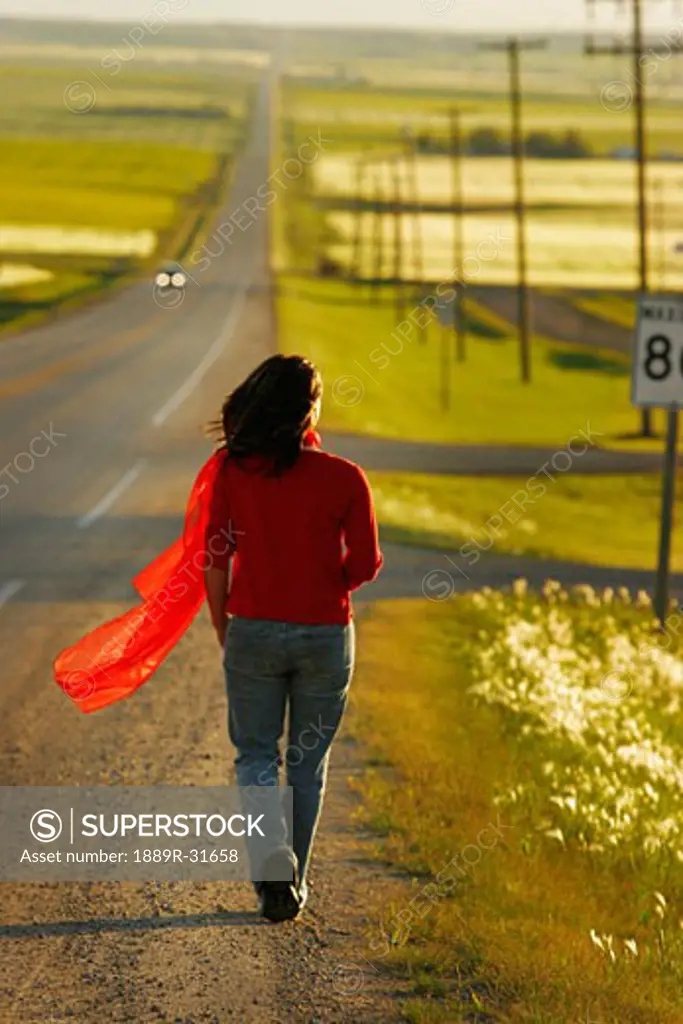 Woman walking along highway surrounded by fields