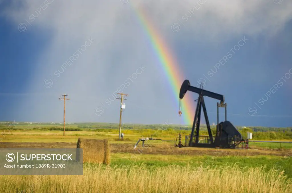 Storm clouds and rainbow over prairie oil pump  