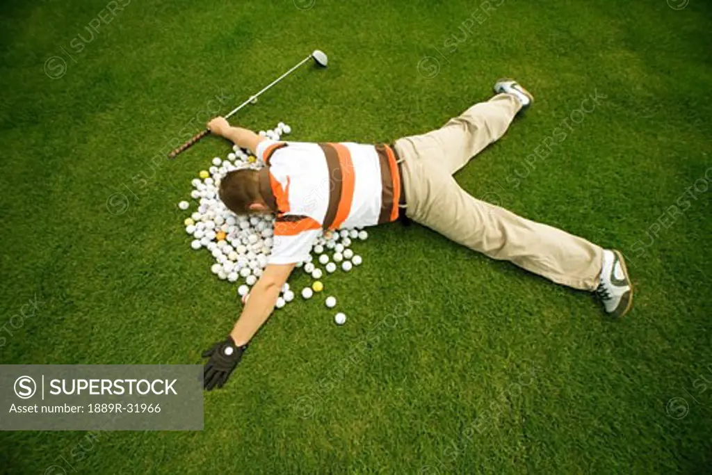 Man holding a golf club and lying on pile of golf balls