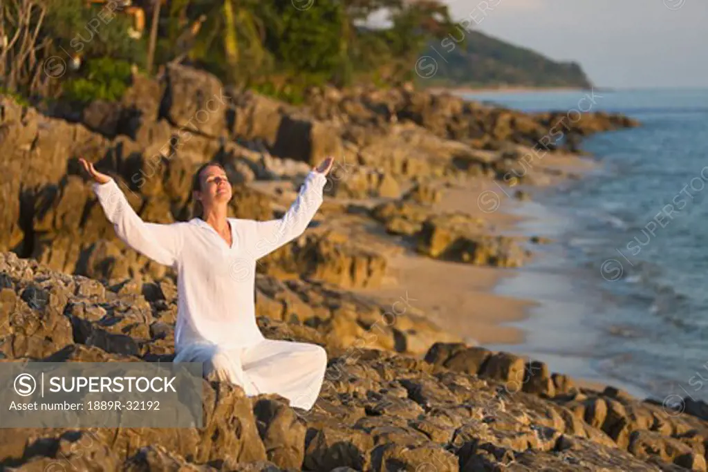 Woman with arms raised on rocky shoreline