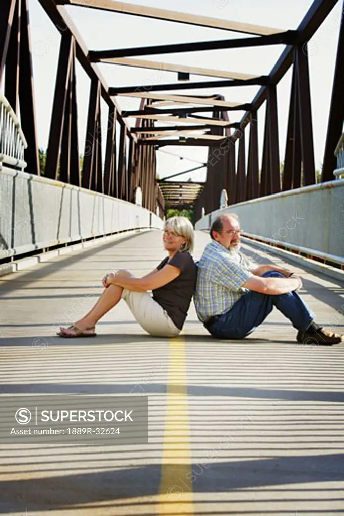 Husband and wife sitting on the middle of a bridge