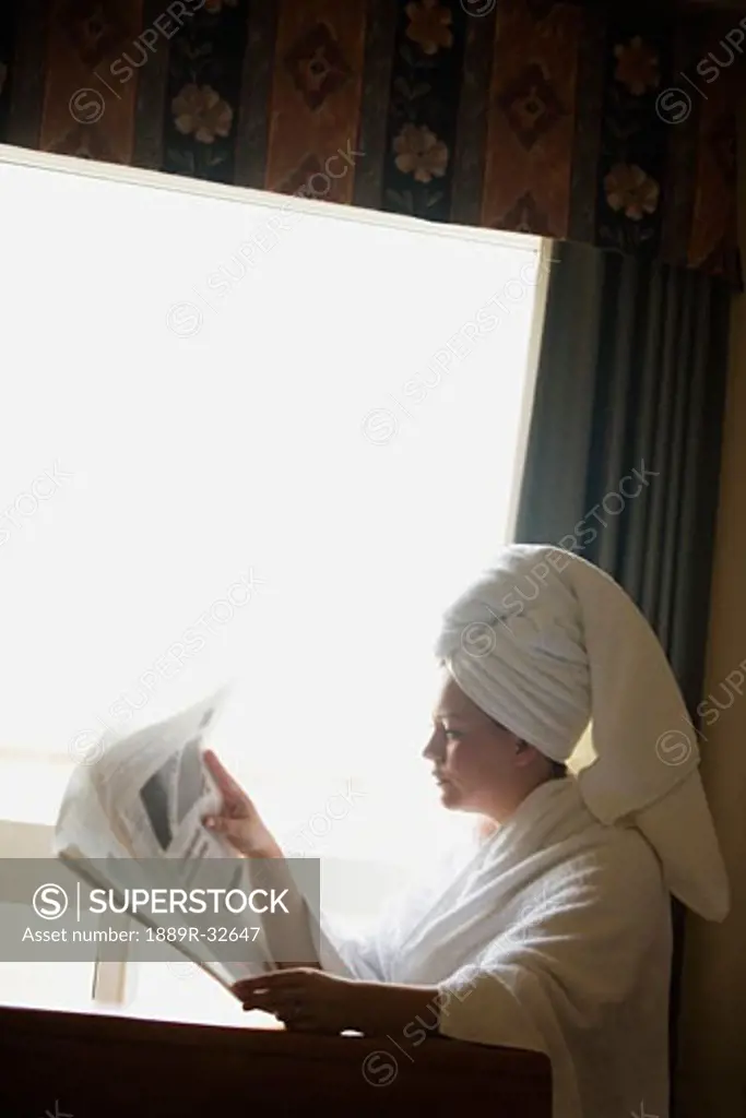 A woman in a bathrobe reading the newspaper