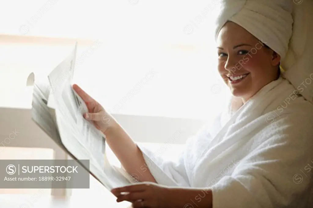 Woman reading newspaper in robe and towel