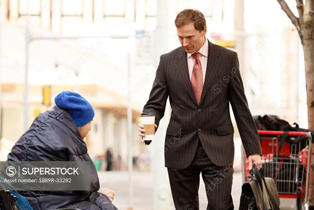 Businessman giving coffee to homeless man