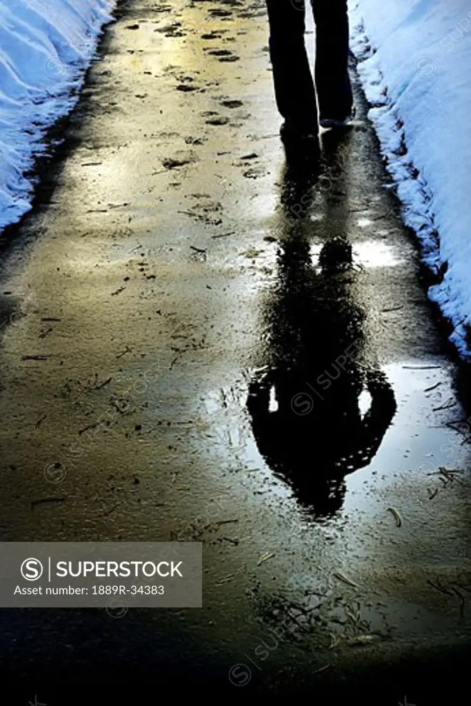 Reflection of person walking on the wet sidewalk