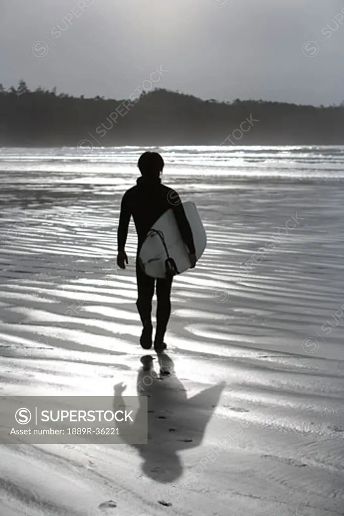 Cox Bay, Tofino, British Columbia, Canada; Surfer walking on the beach