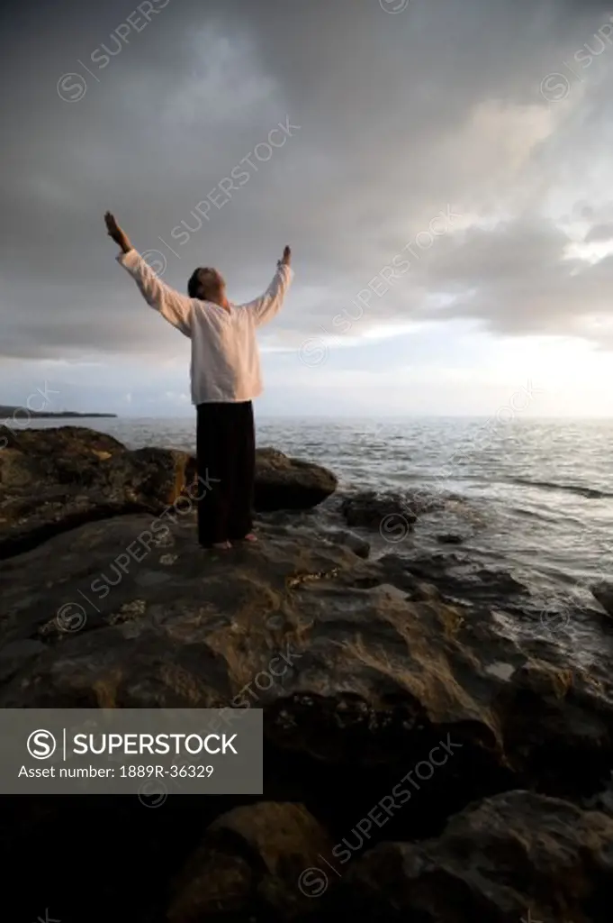 A person with arms raised on a beach at sunset