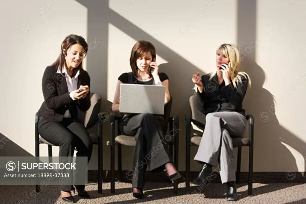 Three women sitting, talking on cell phones