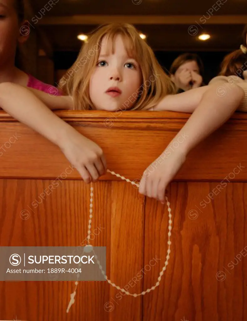 Young girl holding rosary beads over pew