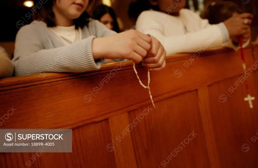 Rosary beads hanging from hands resting on pew