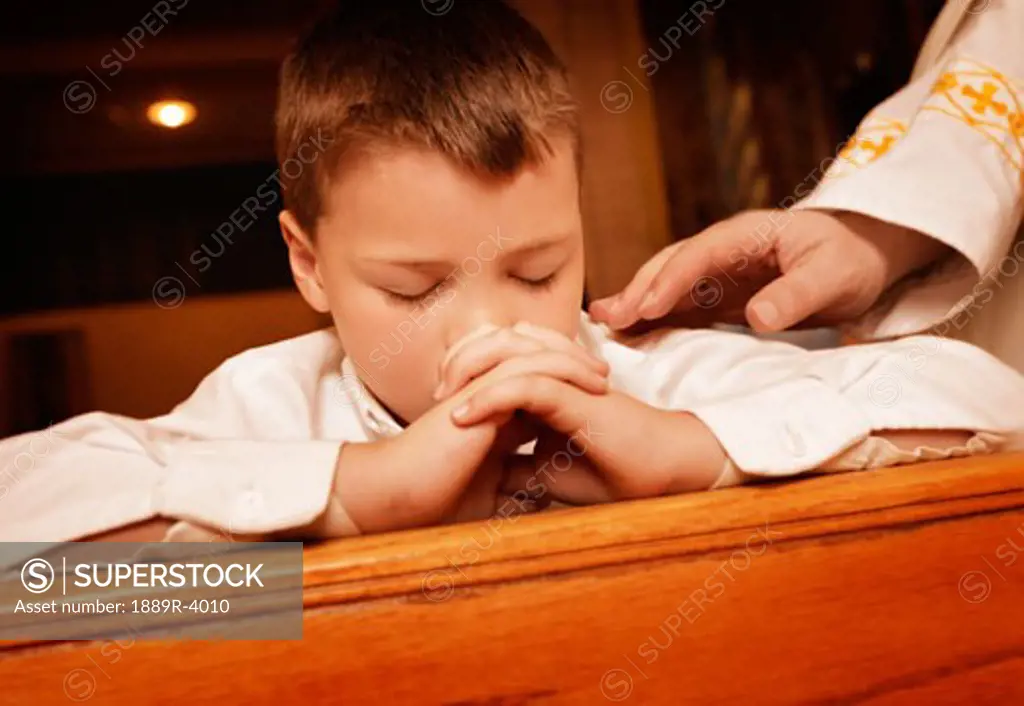 Young boy praying as Priest lays hand on arm