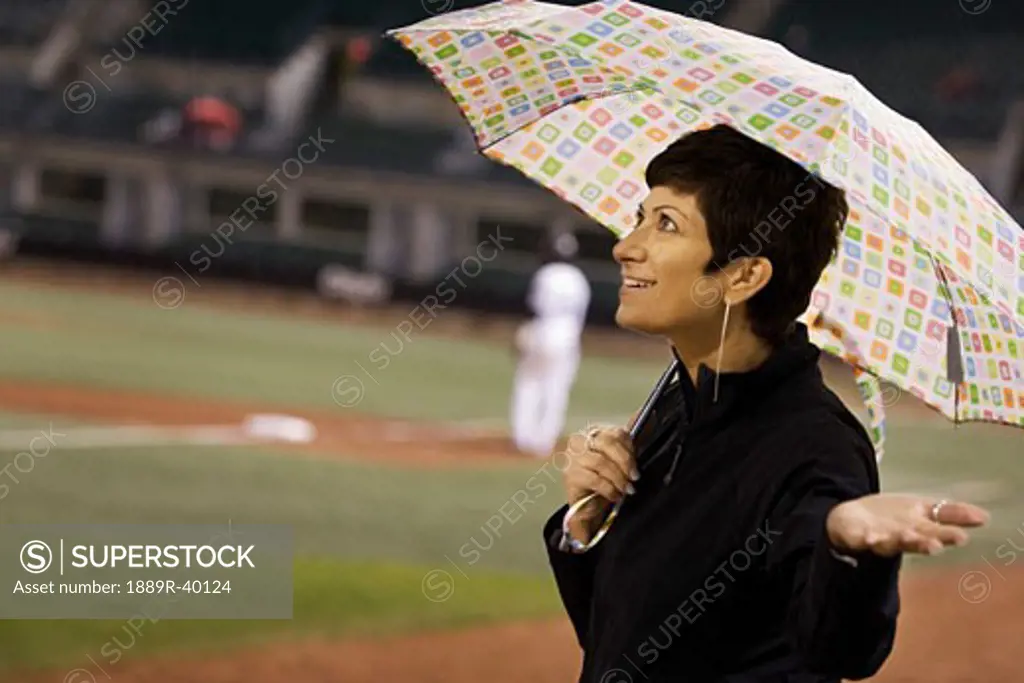 Woman holding an umbrella at a baseball game