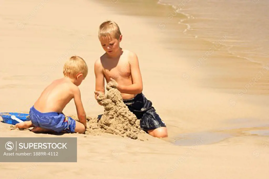 Brothers building sandcastle on beach