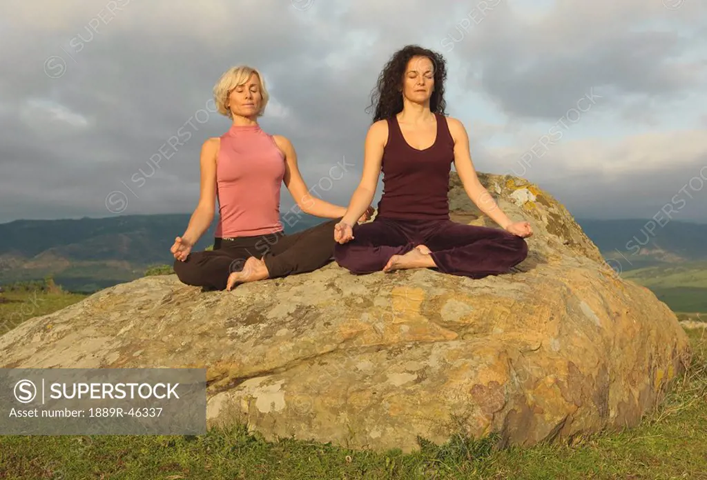 Two women on large boulder in yoga pose
