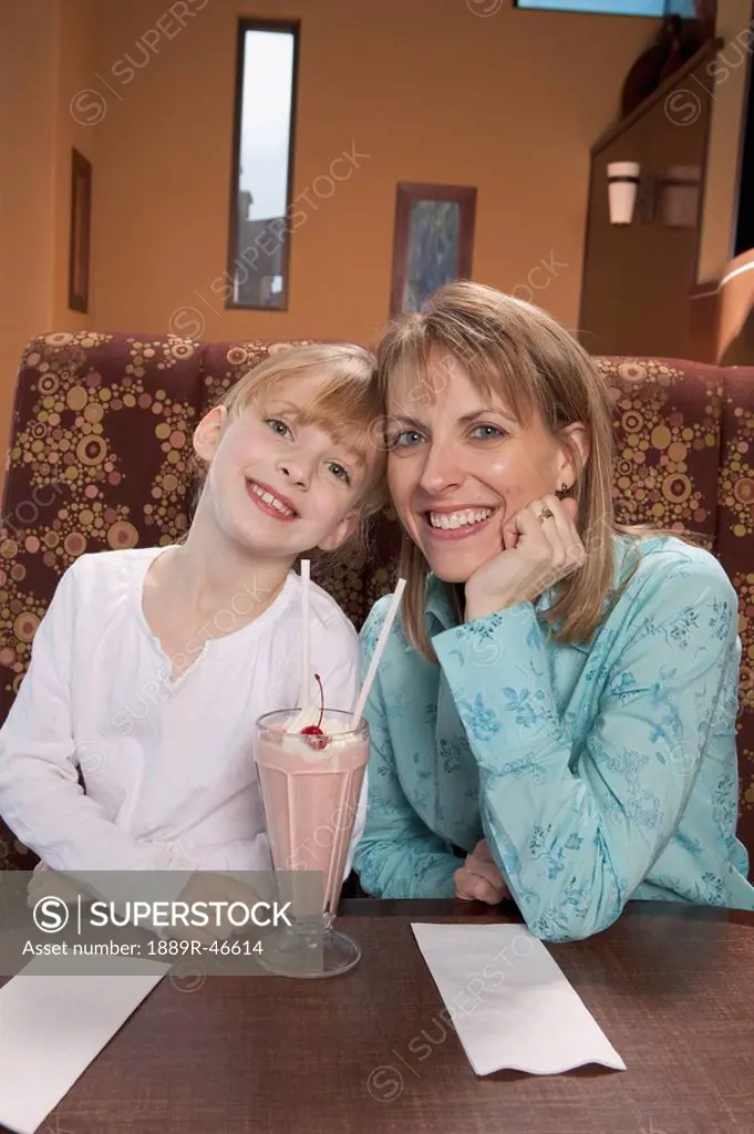 Mother and daughter sharing a strawberry milkshake