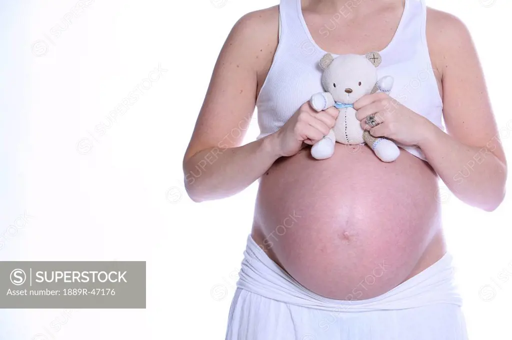 Pregnant woman holding teddy bear over bare belly