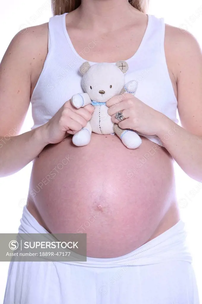 Pregnant woman holding teddy bear on her bare belly