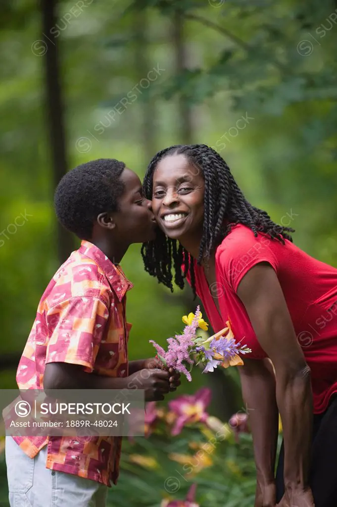 A boy giving his mother flowers and a kiss