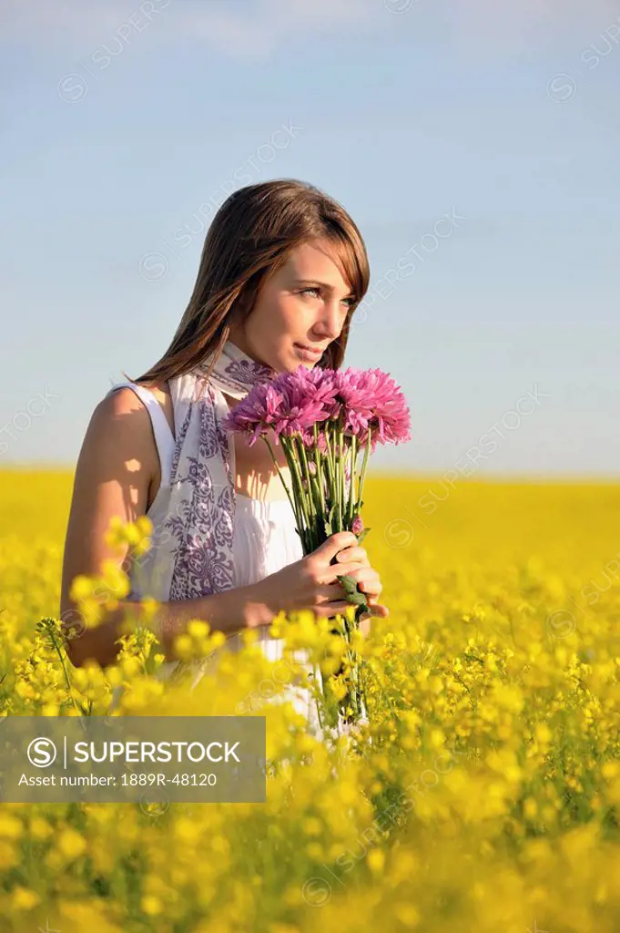 Woman sniffing purple flowers while standing in golden field