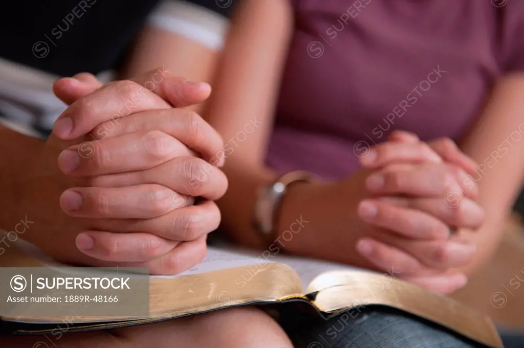 Praying hands of a couple reading the Bible together