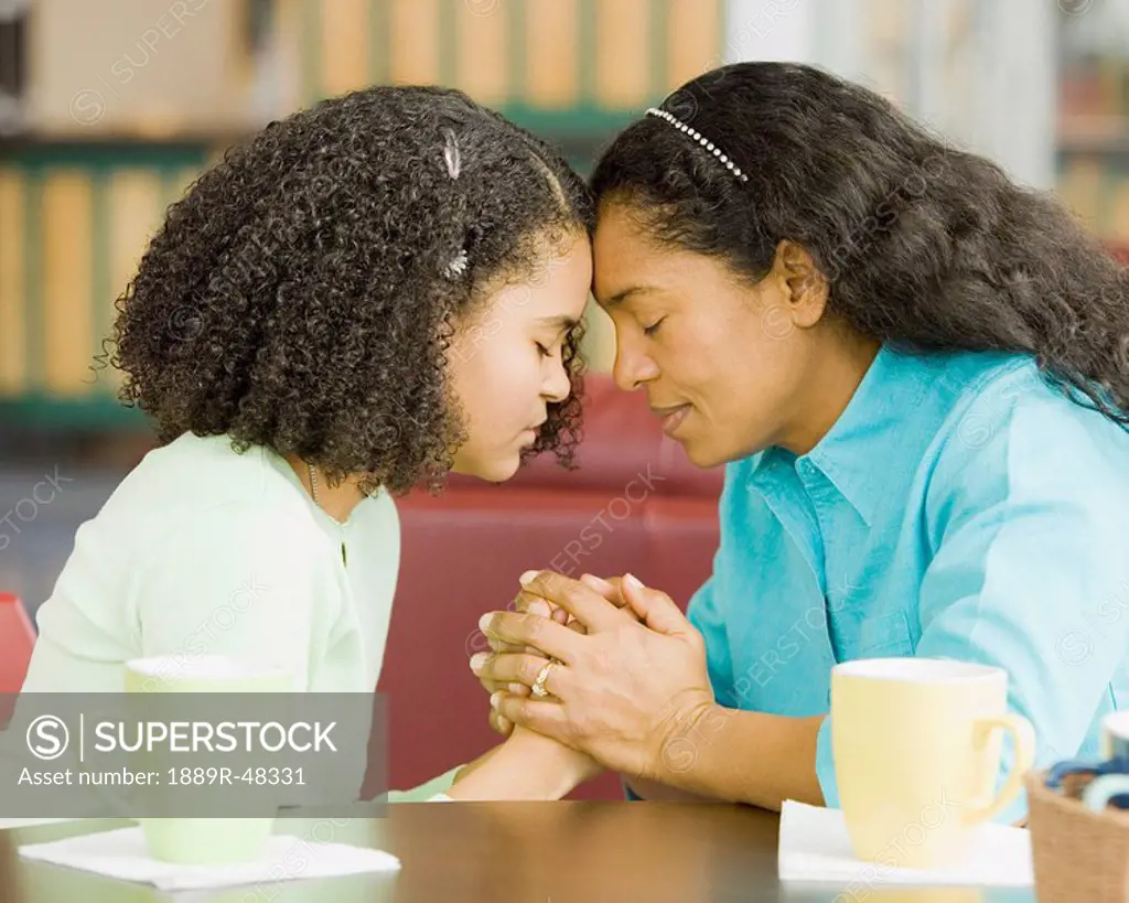 Hispanic mother and daughter praying in coffee shop