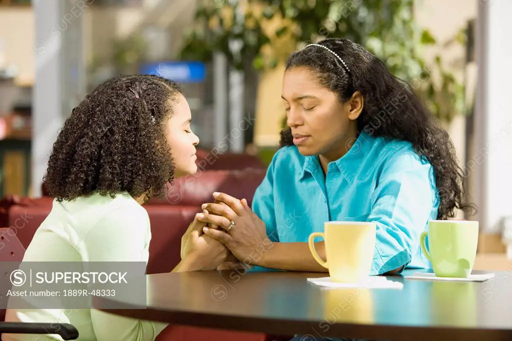 Hispanic mother and daughter praying in coffee shop