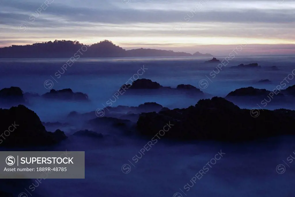 Fog around coastal rocks at twilight