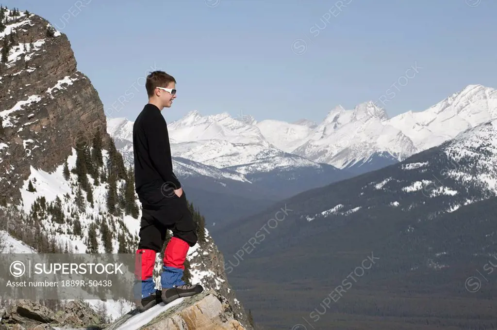 lake louise, banff national park, alberta, canada, a young man standing on a rock ledge overlooking snow_covered mountains and a valley