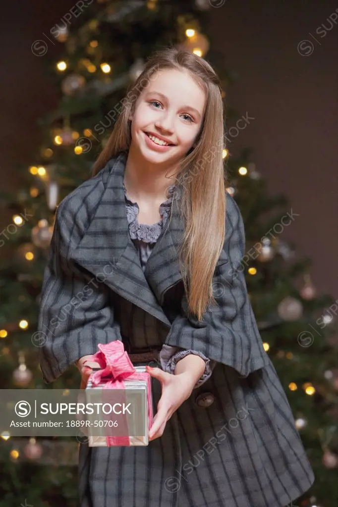 girl holding a gift standing in front of the christmas tree