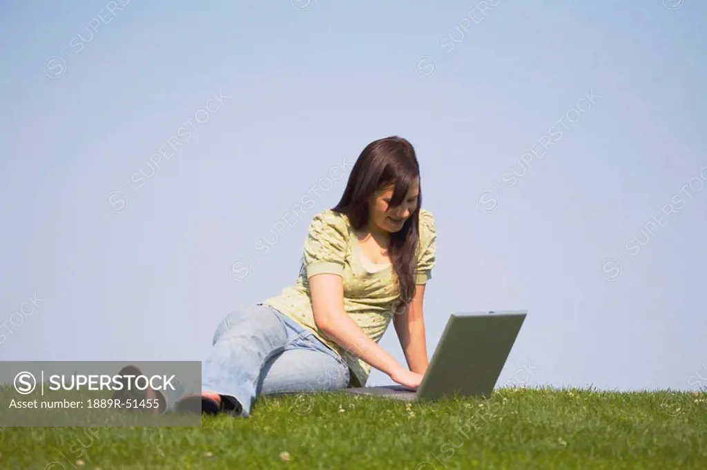 a girl working on her laptop while sitting on the grass