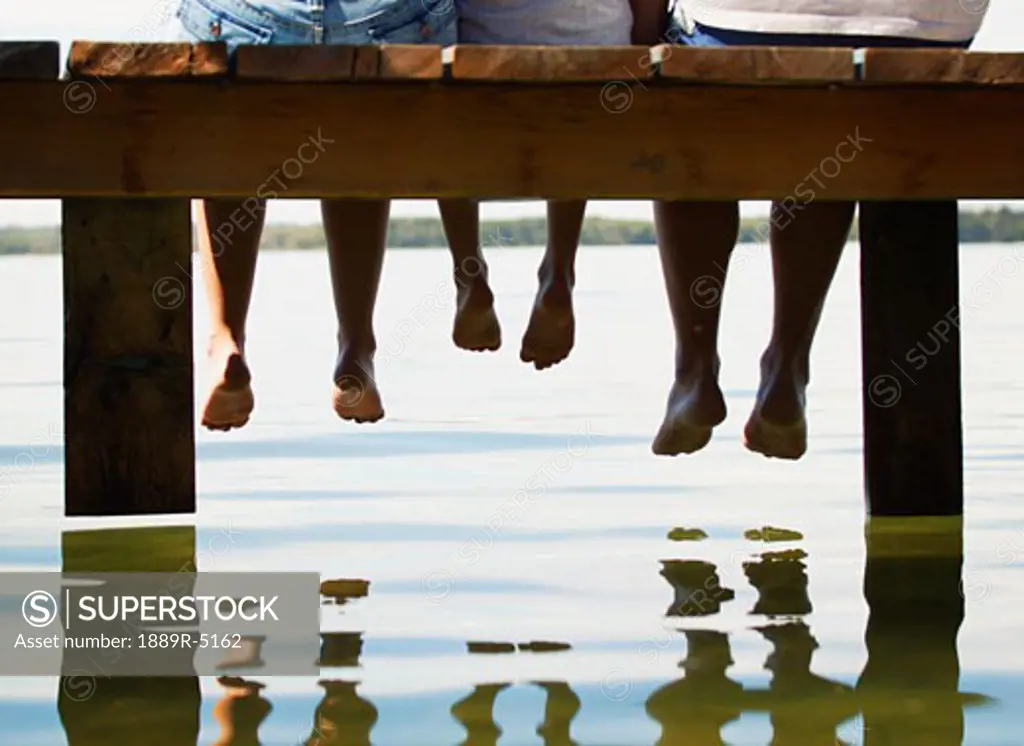 Three people dangling their feet from a dock