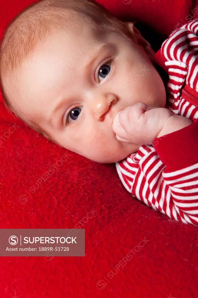 an infant wearing red and white and sucking on her fist