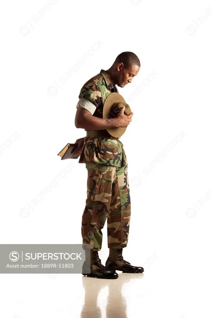 a military man holding his hat and bible and praying
