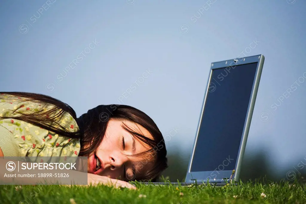 a girl who has fallen asleep on her laptop computer while working in the park