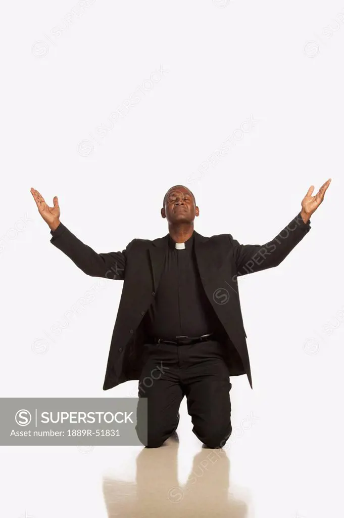 a man wearing a clerical collar and kneeling with hands raised