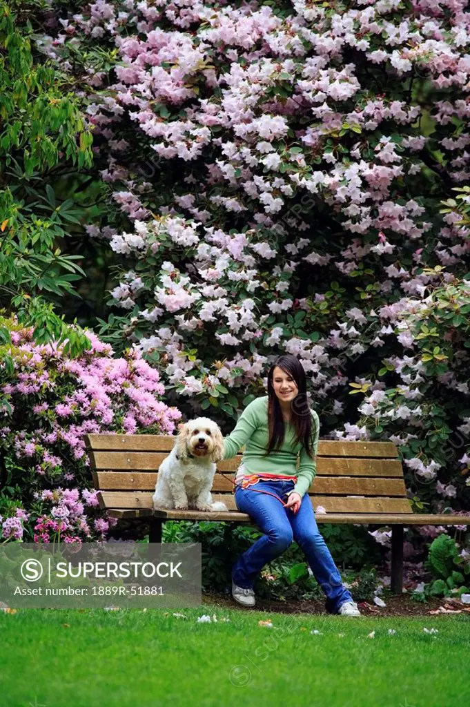 a girl sitting with her dog on a bench in the park