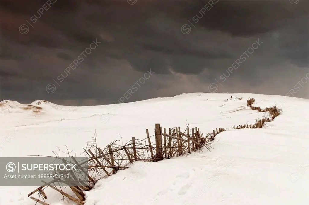 a broken fence in a snowy field with a dark sky above