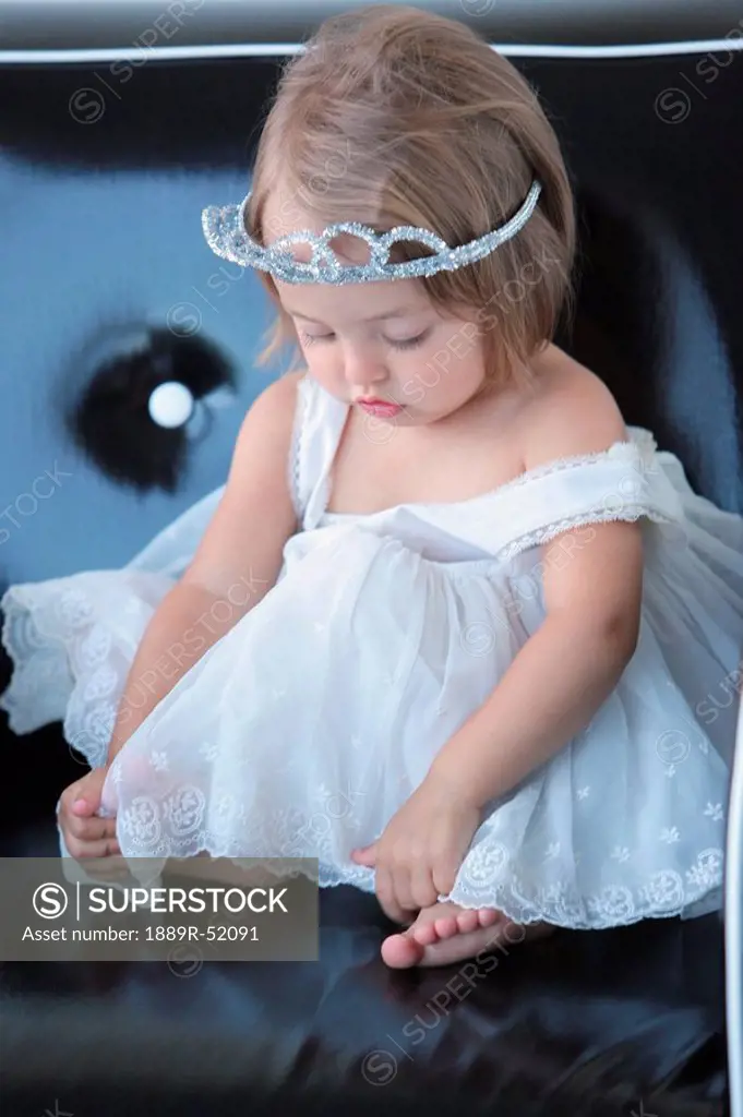 a young girl in a white dress wearing a tiara