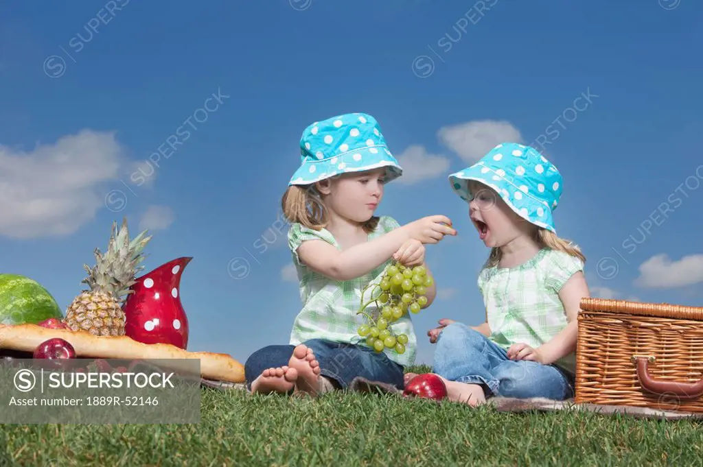 two young girls sharing grapes at a picnic