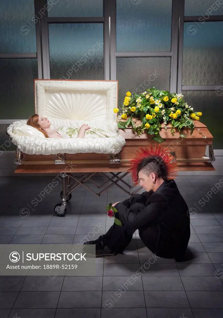 a young man sitting beside a coffin with a young woman´s body in it